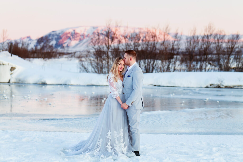 Bröllopsfotograf Island - ett brudpar som står i snön och håller om varandra med en vacker himmel och snötäckta berg i bakgrunden.