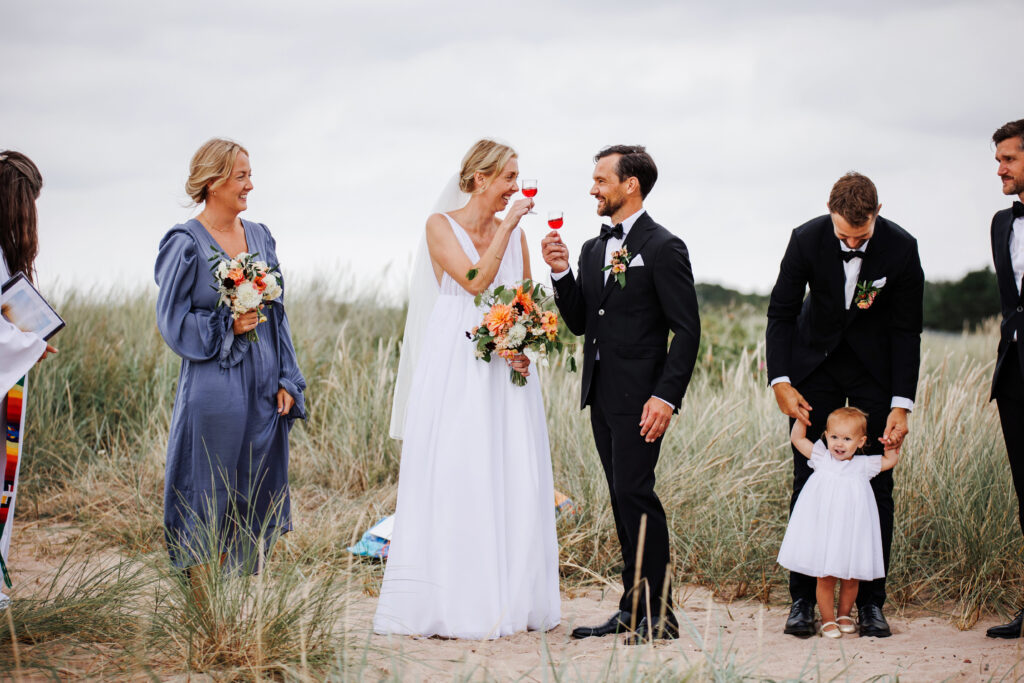 Bröllopsfotograf Skåne - Brudpar under vigseln på stranden som har varsitt glad med dryck skålar med varandra.