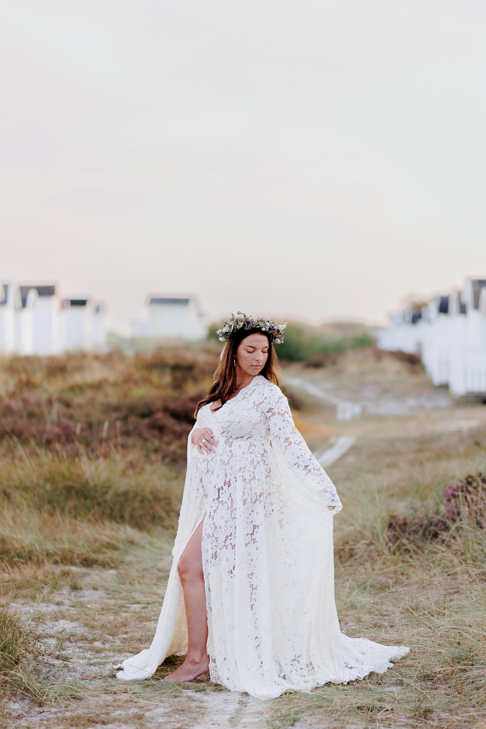 Bellafroy Photography – Din gravidfotograf i Skåne Gravidfotografering Malmö, Gravidfotografering Skåne - gravid kvinna som står bland gräs och strandhytter i en fin klänning.