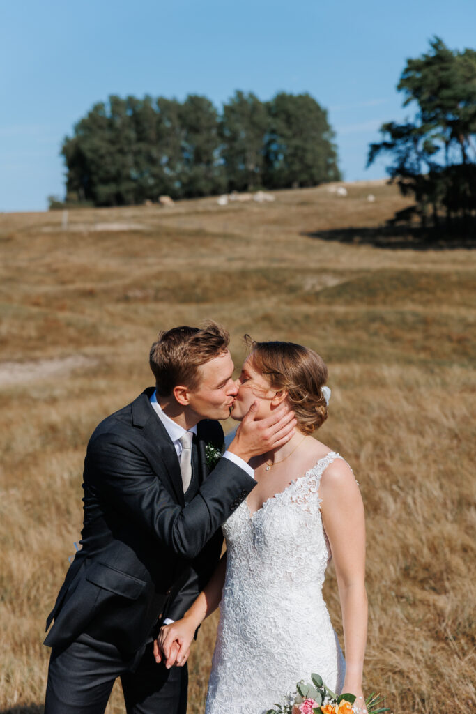 Bröllopsfotograf Skåne - Ett prudpar som kysser varandra på ett öppet fält, halvkroppsbild.